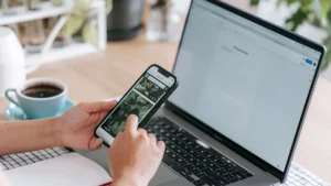 Primera cuenta bancaria online: persona usando el móvil junto al portátil y un café