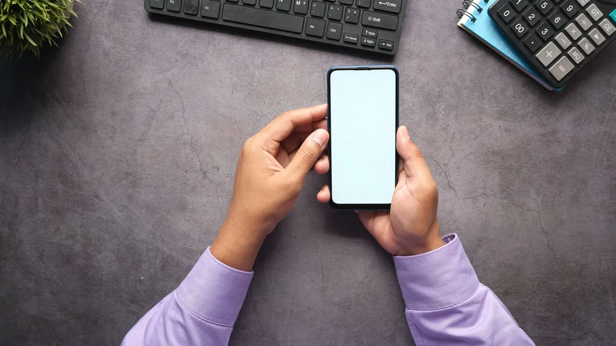 Cambiar de banco desde el móvil: manos con un teléfono junto a una calculadora y una libreta
