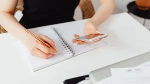 Persona anotando su plan de ahorro en una libreta mientras consulta una app con coaching financiero en el móvil