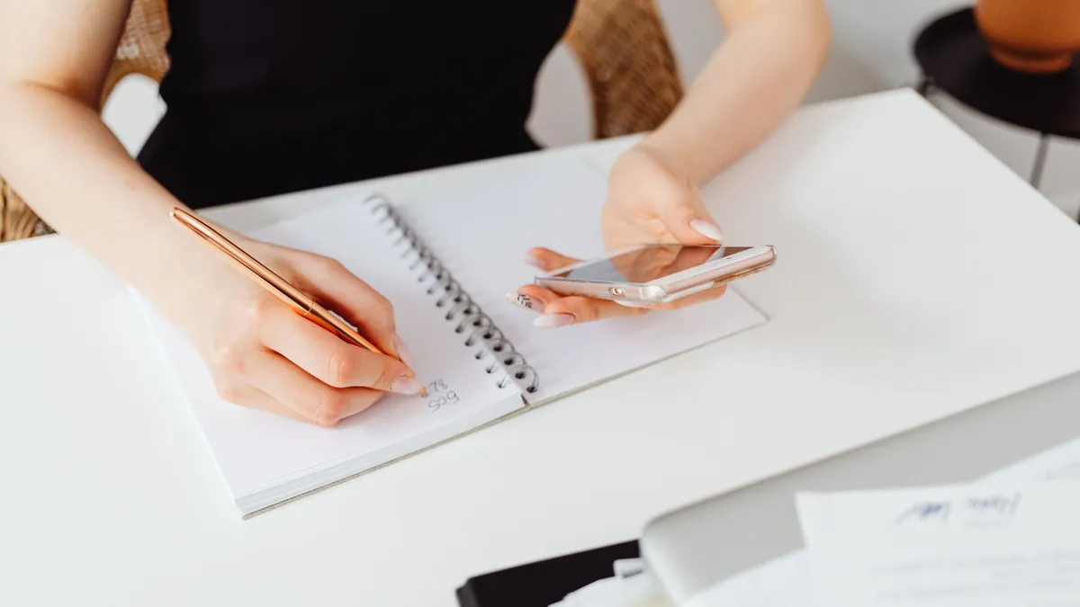 Persona anotando su plan de ahorro en una libreta mientras consulta una app con coaching financiero en el móvil