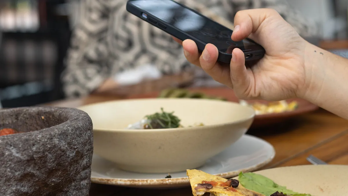 Persona con el móvil en la mesa de un restaurante para dividir la cuenta con Bizum sin superar los límites de Bizum