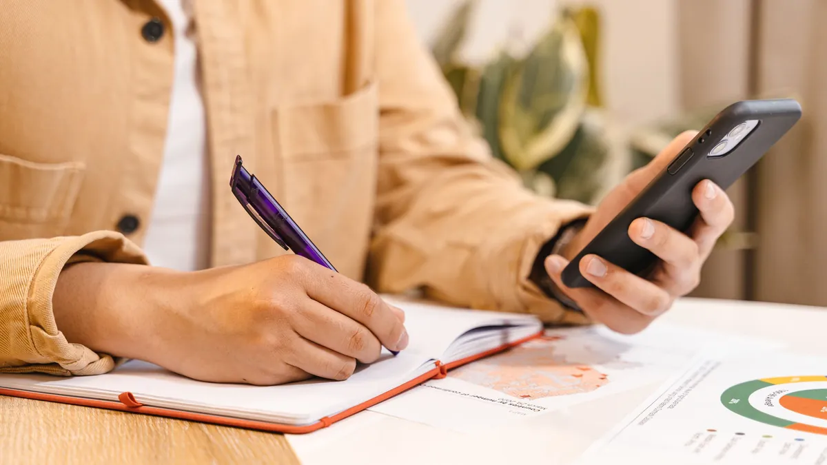Gastos por categorías: persona anotando en una libreta lo que le muestra la app del móvil