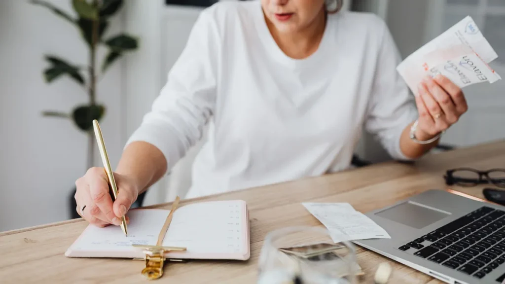 Método 50/30/20: mujer anotando sus gastos mensuales en una agenda con un tique en la mano
