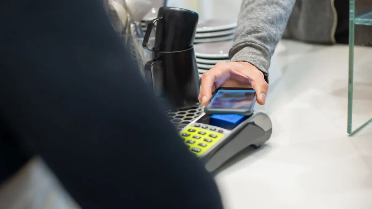 Cliente acercando el móvil al datáfono de una cafetería para pagar con Bizum Pay