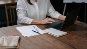 Presupuesto con IA: mujer revisando sus gastos del mes en el portátil con documentos sobre la mesa