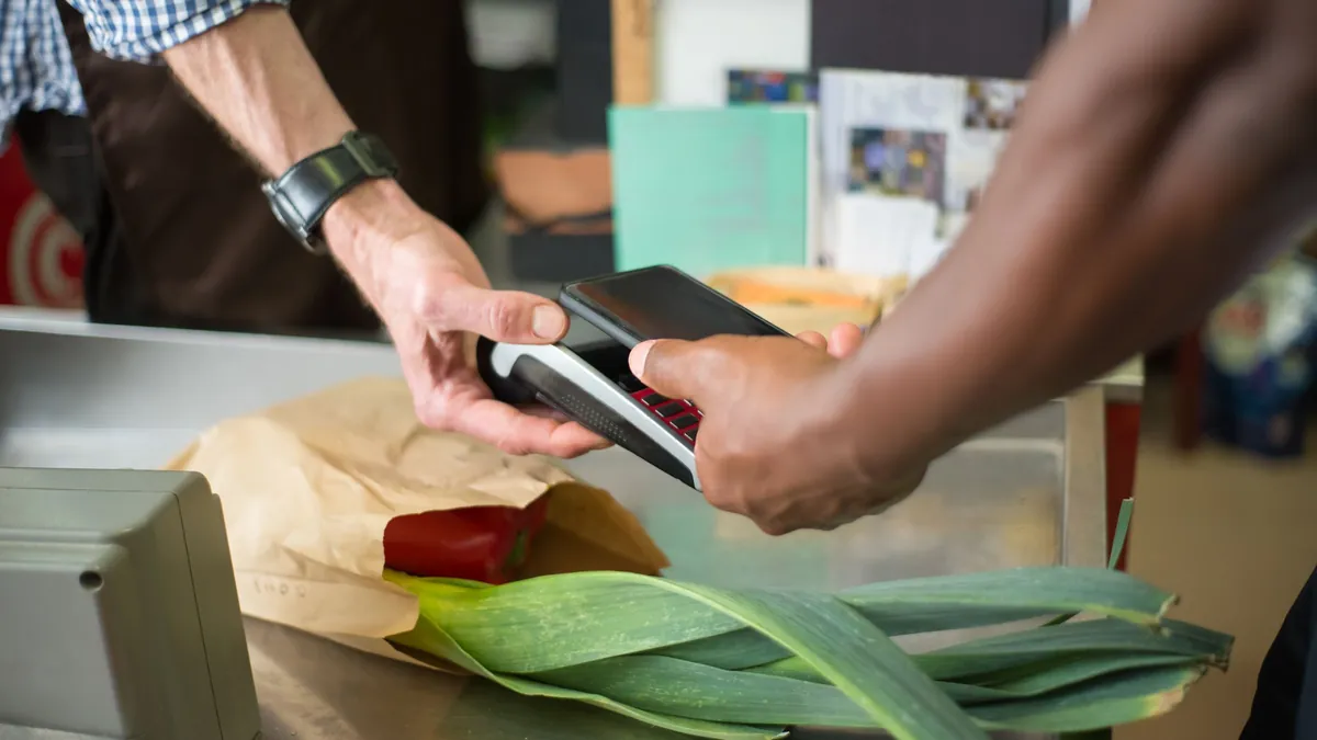 Pago con el móvil en un datáfono al hacer la compra en una frutería